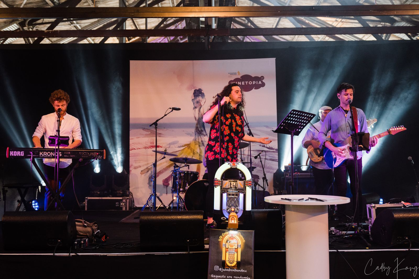 Jukebox Band playing on stage under white light beams with the jukebox front of stage