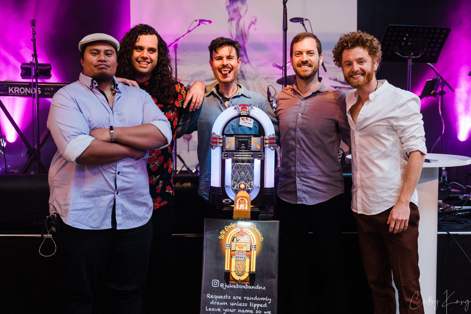 The five members of Jukebox Band standing around the jukebox after a show