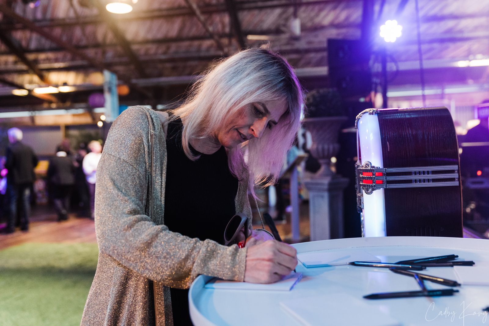 A guest leaning over a table writing a song request on a slip of paper beside the jukebox